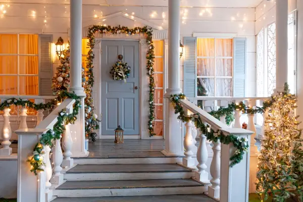 House entrance way and porch of a residential home decorated for the holidays with golden and green wreath garland of fir tree branches and lights. 