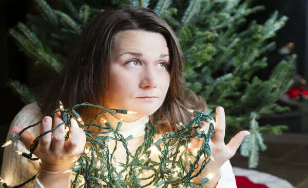 A frustrated person trying to untangle holiday lights in front of a tree.