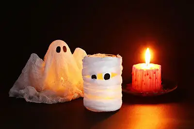 Ghost and mummy decorations sitting next to a lit candle.